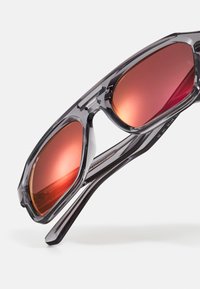 Occhiali da sole con montatura grigia trasparente, lenti ottagonali e lenti riflettenti rosso-arancio, dotati di astine eleganti e hardware minimale.