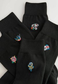 Fünf schwarze Socken mit bestickten bunten Designs, darunter ein Tigerkopf, eine Schlange, eine Rose, ein Totenkopf mit Rose und ein Vogel.