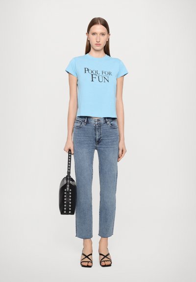 Hellblaues, kurzes T-Shirt mit schwarzem Text "POOL FOR FUN", kombiniert mit hochgeschnittenen blauen Jeans und schwarzen Riemchensandalen. Schwarze Handtasche mit Nieten.
