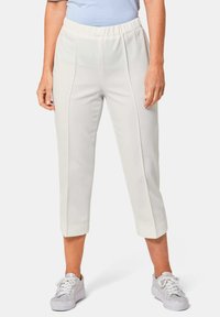 Witte cropped broek met een gestructureerd oppervlak en een elastische tailleband, gecombineerd met lichtgrijze sneakers. De broek heeft details aan de zijnaad.