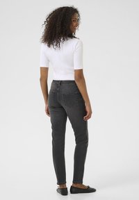 Jean noir taille haute avec une coupe slim, doté de poches arrières et d'un délavage subtil. Associé à un haut ajusté à manches courtes blanc.