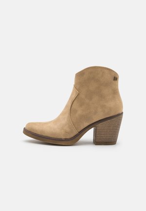 Béžová kotníková bota z broušené kůže s zakřiveným svrškem, zaoblenou špičkou a naskládaným dřevěným podpatkem. Jemné prošití a malý kovový detail jsou viditelné.