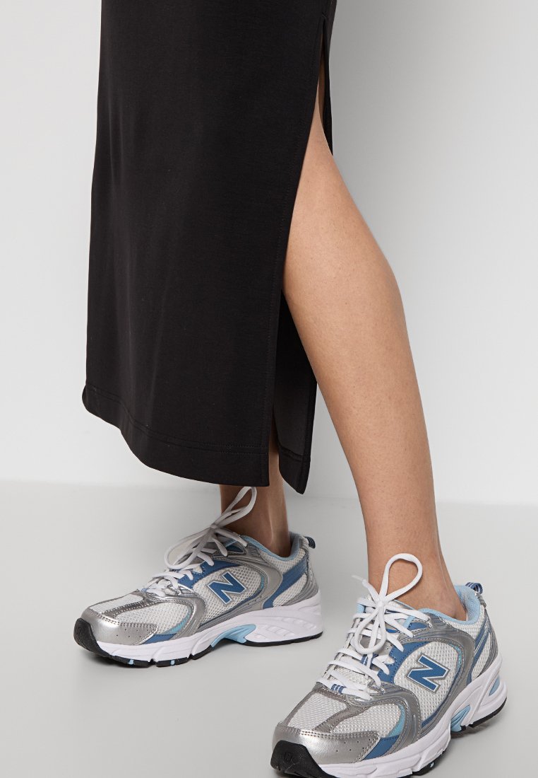 Scarpe da ginnastica argento e blu con dettagli in rete e sintetico. Gonna nera al ginocchio con spacchi laterali. Design minimalista, profilo elegante.