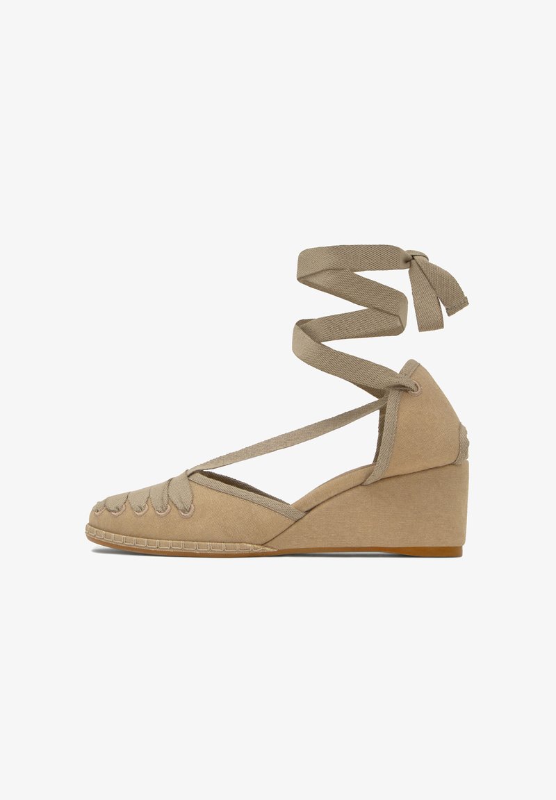 Espadrille compensée beige avec bout fermé, détails cousus, et liens à nouer autour de la cheville, en toile, avec un talon de hauteur modérée.