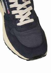 Primo piano di una scarpa sportiva blu navy con lacci beige, punta in mesh, sovrapposizione in suede e intersuola color crema.