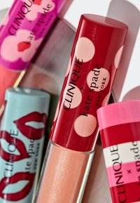 Vier lipgloss-tubes: één rood met roze stippen, één lichtroze, één teal met lippenafdruk en één felroze met horizontale strepen.