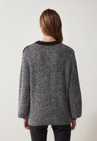 Strikket genser i svart og grått med et teksturert mønster. Har en svart ribbestrikket halsringning og mansjetter, samt design med senket skulder.