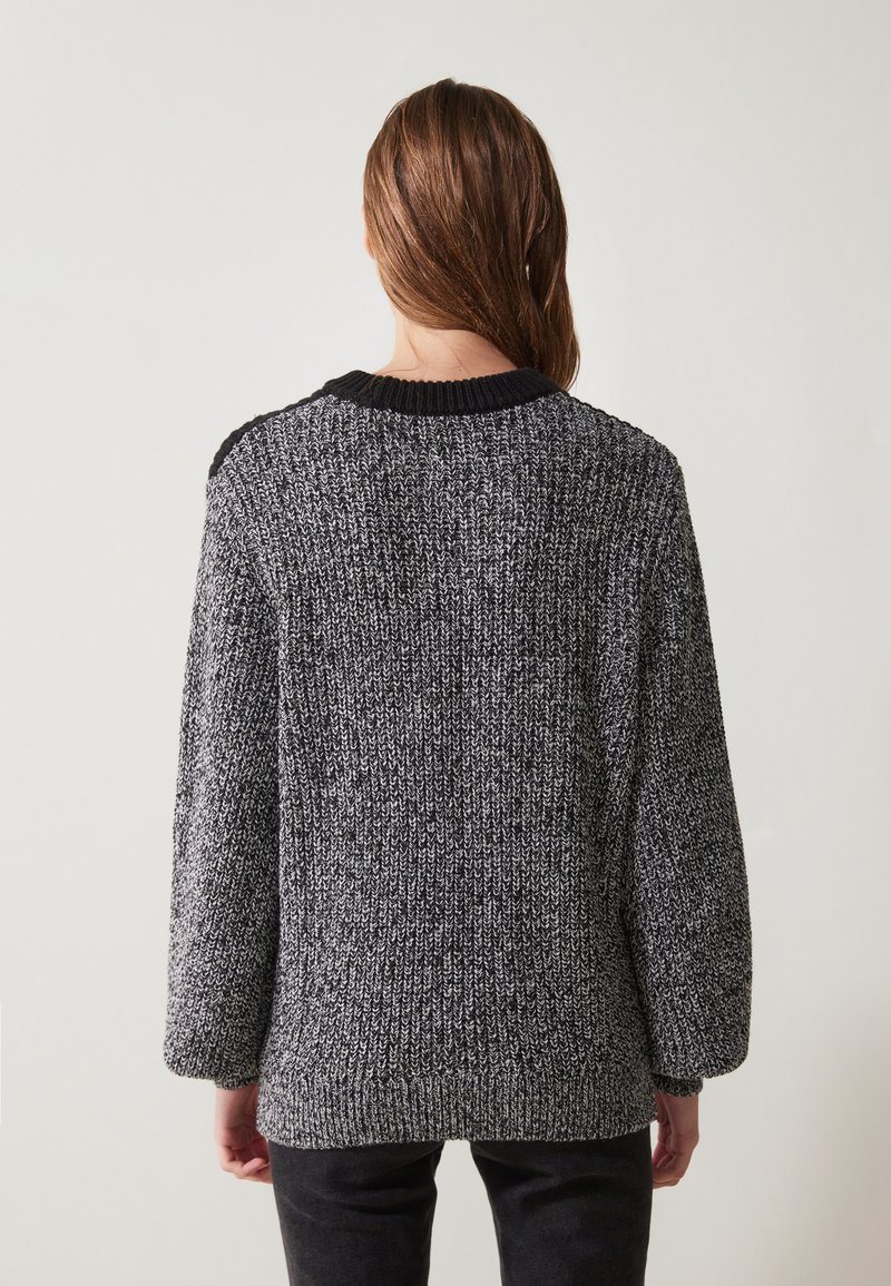 Sweter dzianinowy w kolorze czarnym i szarym z teksturowanym wzorem. Posiada czarną prążkowaną linię dekoltu i mankietów oraz opadające ramiona.