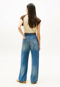 Jeans w szerokich nogawkach w jasnoniebieskim denimu z detalami w efekcie wyblaknięcia, połączone z beżową bluzką z krótkim rękawem w brązowe wzory. Gładka tekstura.