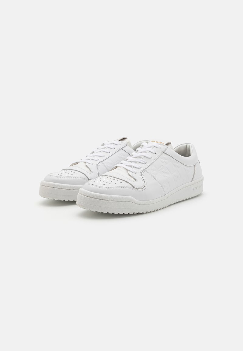White leather sneakers with perforated toe, subtle logo design, flat rubber sole, and matching laces. Smooth texture with minimal accents.