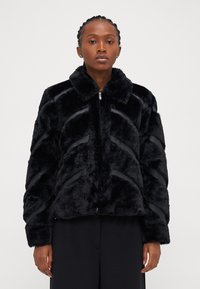 Μαύρο ψεύτικο παλτό από γούνα με κλείσιμο με φερμουάρ, διαθέτει γιακά και σχέδιο σε σχήμα βέλους, υφασμάτινη υφή και ρέγουλες στις μανσέτες.