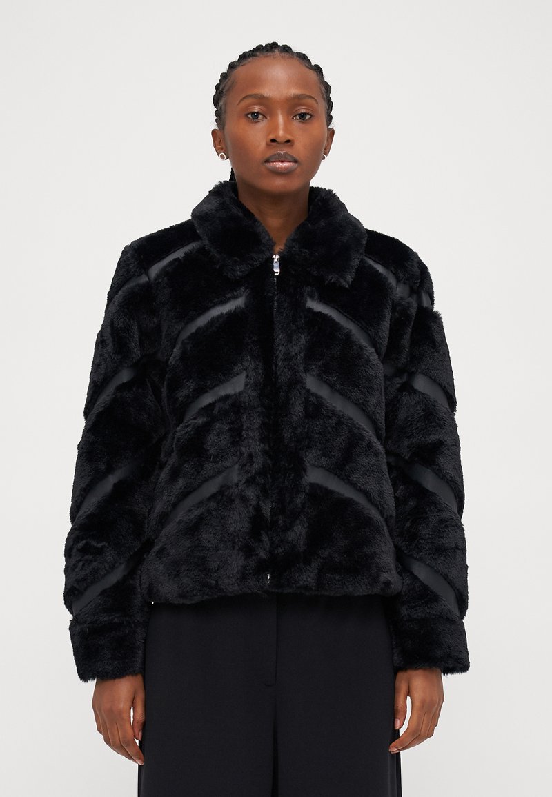 Μαύρο ψεύτικο παλτό από γούνα με κλείσιμο με φερμουάρ, διαθέτει γιακά και σχέδιο σε σχήμα βέλους, υφασμάτινη υφή και ρέγουλες στις μανσέτες.