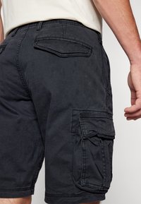 Black cargo shorts featuring side and back pockets, made from durable fabric with a smooth texture and stitched seams.