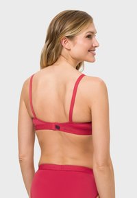 Red bra with thin straps and a hook closure at the back, featuring a smooth texture and contrasting dark accents on the band.