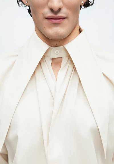 Cream shirt featuring a high collar with a button closure, vertical pleats, and smooth texture, with a prominent draped design.