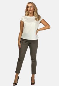 Jasno beżowa bluzka z krótkim rękawem zestawiona z dopasowanymi spodniami w kolorze oliwkowym, noszona z czarnymi sandałami na wysokim obcasie. Gładki materiał, wyraźne linie.