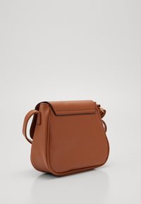 Ruskea keinonahkainen olkapussukka, jossa on jämäkkä muoto, yläkansi ja irrotettava olkahihna. Sileä pinta ja hienovaraiset ompeleet.