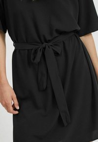 Svart klänning med lös passform, korta ärmar och en knuten midjebälte. Slät tyg med mjuk textur och minimalistisk design.