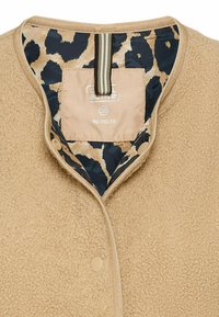 Die Innenseite der beigen Fleecejacke zeigt ein Leopardenmuster-Futter, mit einem Etikett, das "recycelt" und die Größe 38 anzeigt, und einem gestreiften Aufhänger.