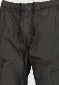 Pantaloni cargo grigi scuri realizzati in tessuto leggero. Presentano una vita con coulisse e cuciture arancioni a contrasto, oltre a tasche laterali.