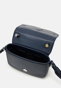 Granatowa skórzana torebka przez ramię z magnetycznym zapięciem, teksturowanym wykończeniem i regulowanym paskiem; zawiera wewnętrzną przegródkę.