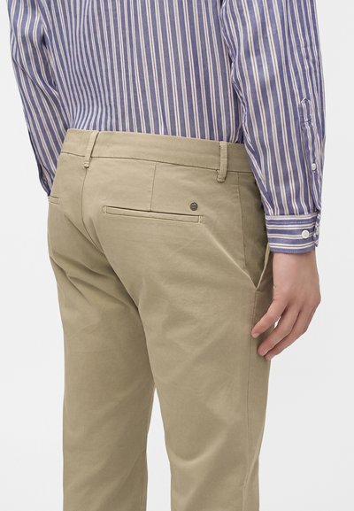 Homme portant un pantalon beige et une chemise à manches longues rayée verticale bleue et blanche, vu de dos de la taille vers le bas.