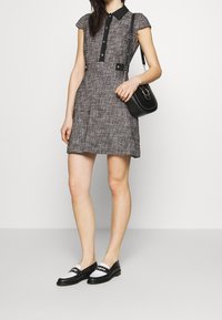 Czarna i biała sukienka w kratę z krótkimi rękawami, zapięciem przy kołnierzyku i dopasowaną talią. Czarna torebka na ramię i czarne mokasyny z białymi akcentami.