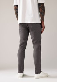 Szare bawełniane spodnie o dopasowanym kroju, z detalicznym przeszyciem i gładką fakturą. Noszone z luźną białą koszulką i białymi sportowymi butami.