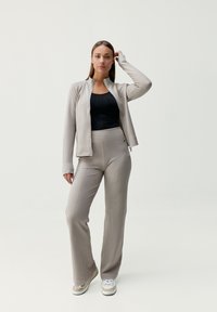 Beige zipová bunda přes černý přiléhavý top, spárovaná s béžovými kalhotami s vysokým pasem a švy. Celkový vzhled doplňují pohodlné tenisky.