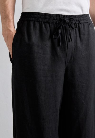 Pantalones de lino negros con cinturilla elástica y cordón, con bolsillos laterales y una tela suave y texturizada.