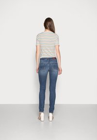 Jean skinny en denim bleu moyen, présentant un design classique à cinq poches, un léger délavage et une étiquette en cuir brun à la taille.