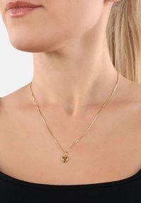 Collana d'oro con una catena sottile e delicata e un pendente a forma di cuore, caratterizzato da una superficie lucida e un piccolo accento rosso lucido.