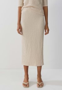 Beige Strick-Midi-Rock aus strukturiertem, zerknittertem Stoff, taillierte Silhouette und geradem Saum, getragen mit hellen Flip-Flops.