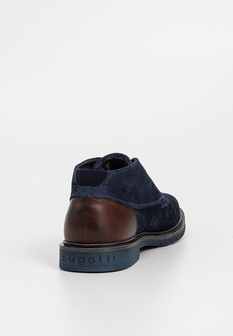 Marineblaue Wildlederschuhe mit einem braunen Lederabsatz. Sie zeichnen sich durch eine glatte Textur und einen leichten Glanz aus, ergänzt durch eine kontrastierende blaue Gummisohle.