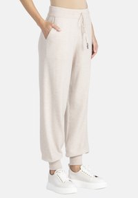 Jasno-beżowe spodnie dresowe wykonane z miękkiej dzianiny, z prążkowanymi mankietami, regulowanym ściągaczem w pasie oraz bocznymi kieszeniami dla większej funkcjonalności.
