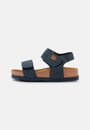 Modre sandale iz sintetičnega materiala z nastavljivimi Velcro trakovi, plitvo podplatom iz plute in gumo z deljeno površino.