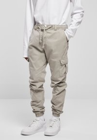 Beige Cargo-Hosen mit einem elastischen Bund, verstellbarem Kordelzug, elastischen Knöchelbündchen und mehreren Seitentaschen. Getragen mit weißen Sneakern.