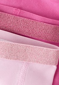 Zestaw trzech legginsów w różnych odcieniach różu, z teksturowanymi elastycznymi pasami i gładką tkaniną z subtelnymi detalami szwów.