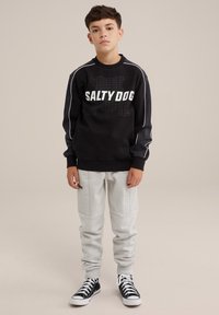 Sweat-shirt noir avec logo "SALTY DOG" blanc, pantalons de survêtement gris et baskets noires. Présente des rayures blanches sur les manches.