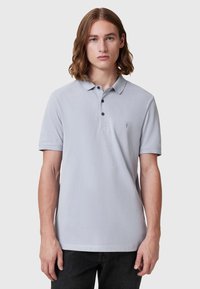 Lys grå polo-shirt med krage, tre-knappers lukking, korte ermer og en liten brodert logo på brystet.