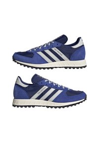 Modré sportovní boty se svrškem z semiše a síťoviny, bílé pruhy, šedé tkaničky, polstrovaný límec a texturovaná černá podrážka. Design ve vintage stylu.