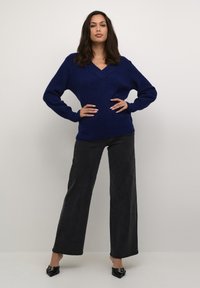 Pulover tricotat navy cu decolteu în V, mâneci lungi și țesătură texturată. Asortat cu blugi negri cu talie înaltă și pantofi negri cu vârf ascuțit.