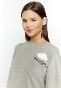 Felpa grigia chiaro con ricamo di una nuvola con bordo rosa, accompagnata da testo in filo blu. Tessuto morbido e vestibilità comoda.