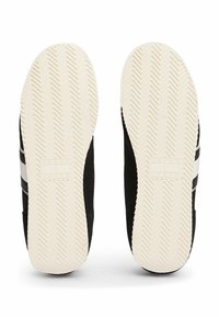 Schwarze Sneakers mit Gummisohlen, ausgestattet mit einem Fischgrätmuster, weißen Streifen und einem strukturierten Obermaterial, das mit "TOMMY JEANS" beschriftet ist.