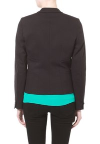 Schwarze maßgeschneiderte Jacke mit figurschmeichelndem Design, ausgestattet mit einem einzelnen Rückenventil. Kombiniert mit einer leuchtend türkisfarbenen Bluse darunter.