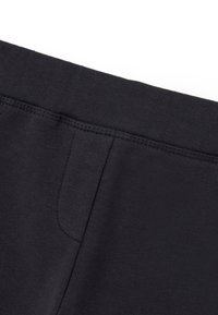 Schwarze Sweatpants aus einem weichen, strukturierten Stoff, mit einem breiten Bund und einer Seitentasche. Nähte sind entlang der Säume sichtbar.