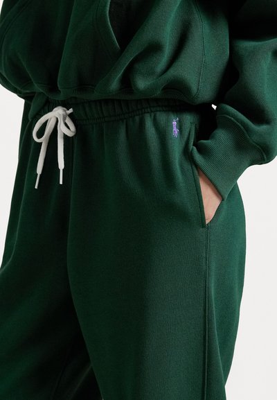 Green sweatshirt with a relaxed fit, featuring a drawstring waistband and side pockets. Notable purple logo on the left. Made from soft fabric.