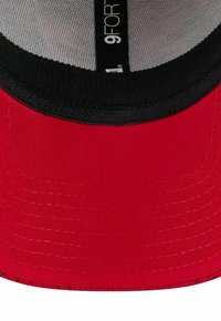 Nahaufnahme des Schirms einer roten Baseballmütze mit schwarzem Innenfutter und einem "9FOr"-Label auf dem inneren Netzpaneel.