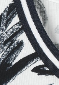 Crewneck top met een witte achtergrond en zwarte abstracte patronen, omrand met een donkerblauwe ribbelkraag met witte strepen.