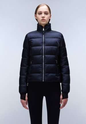 Zwarte pufferjack met hoge kraag, horizontaal gestikt patroon, ritssluiting aan de voorkant en zijzakken; gecombineerd met aansluitende zwarte leggings.